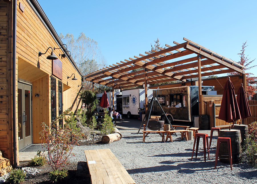 The outdoor patio of Crosscut Taphouse featuring bench seats, several food trucks, and custom trellises